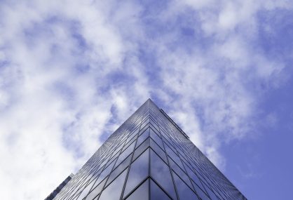 A low angle shot of a tall glass skyscraper business building with cloudy sky in the background