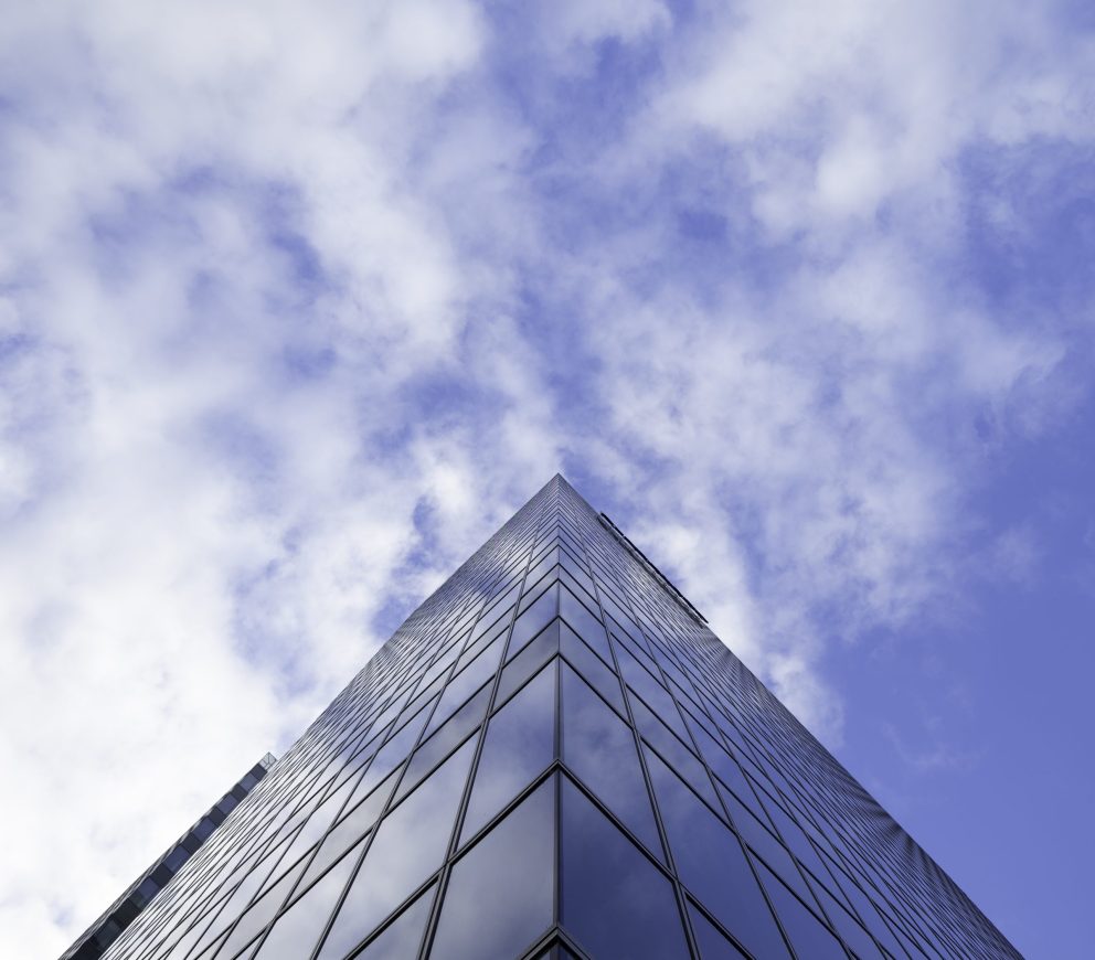 A low angle shot of a tall glass skyscraper business building with cloudy sky in the background
